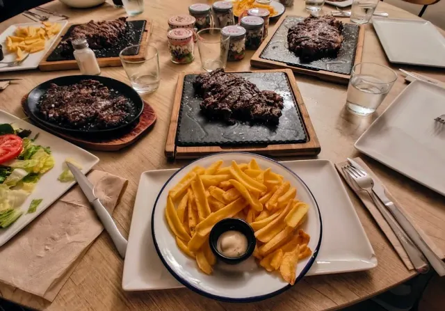 A table loaded with cuts of meat on stone boards, a plate of fries and a vegetable salad