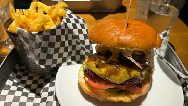 A burger with a skewer and a metal basket full of thick fries, on a tray