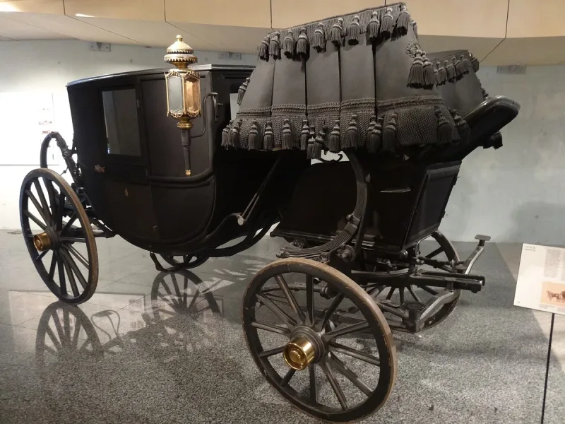 Antique black funeral carriage with a lantern on display in a gallery