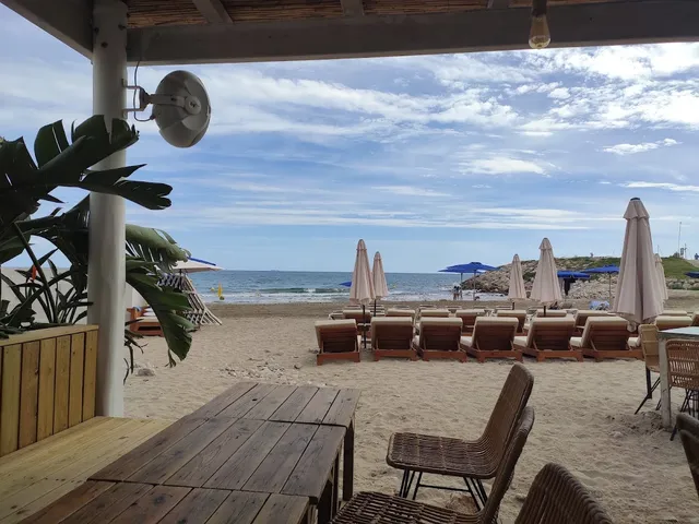 A wooden table under a shelter facing a beach with sun loungers and parasols