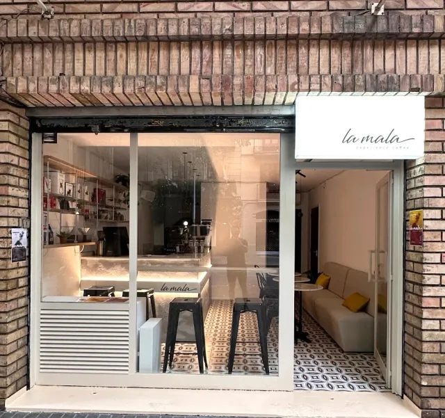 A glass front in a brick wall with a white sign, stools and patterned tiles inside