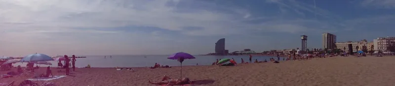 Sandy beach with a purple parasol and a sail shaped hotel on the horizon