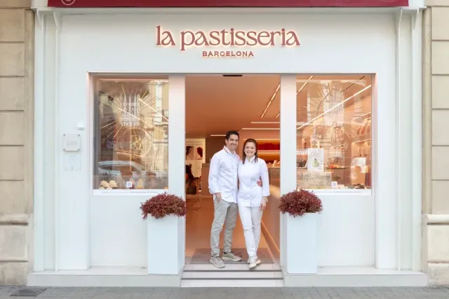 A white facade with display windows, two people in white in the doorway and flower planters