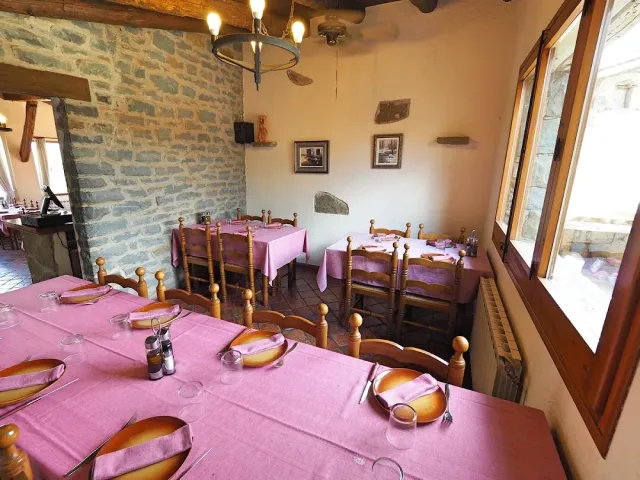 A rustic dining room with a stone wall, pink cloths and carved wooden chairs