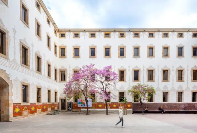 A paved courtyard enclosed by a white facade with rows of windows, and trees blooming in pink