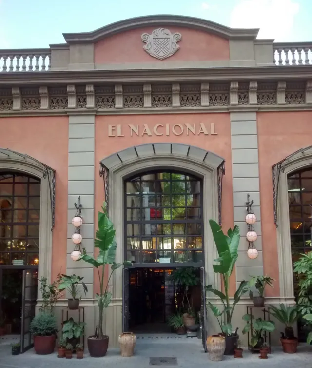 A pink facade with a stone arch, hanging globe lamps and potted palms at the entrance