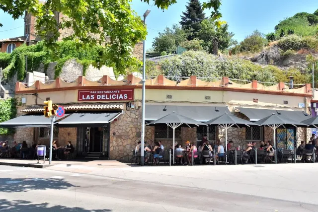 A restaurant in a stone wall with gray parasols and diners outside beside the road