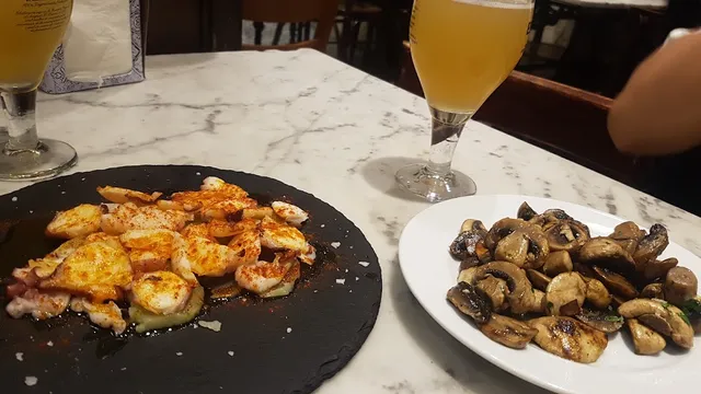 Grilled seafood with paprika and sautéed mushrooms on a marble table, beside glasses of beer