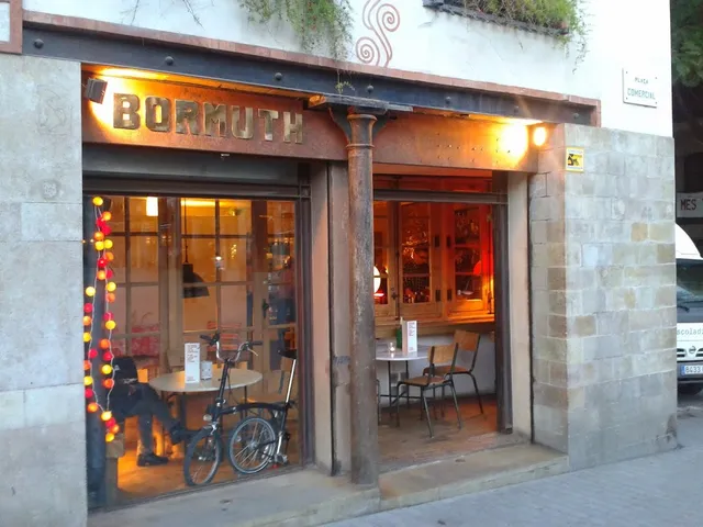 A corner stone frontage with a lit wooden sign, a string of lights and a bicycle in the window
