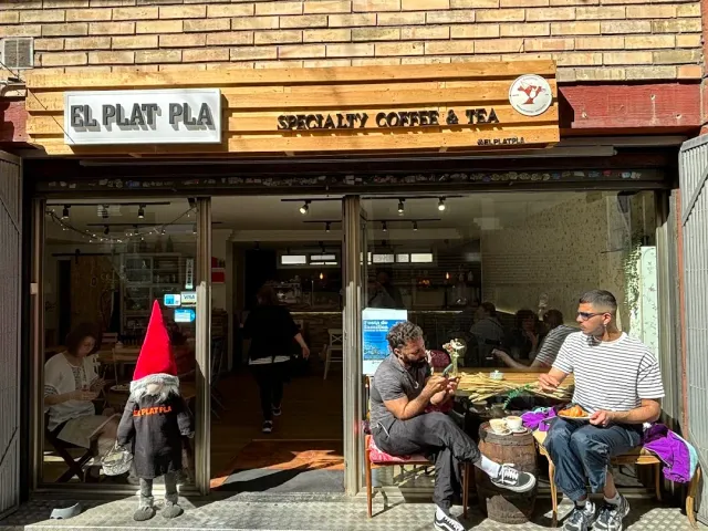 An open front with a wooden sign, people sitting on benches outside and a gnome statue at the entrance