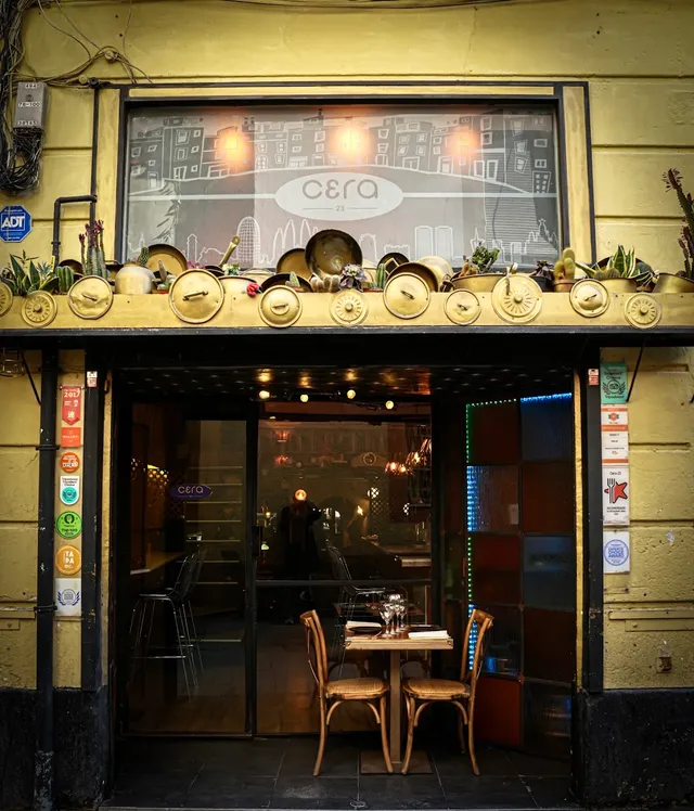 A yellow frontage with copper pots and cacti above the entrance, and a table for two in the doorway