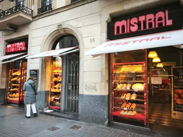 Pastry shelves lit in red in the windows of a street shop, with a passerby looking on