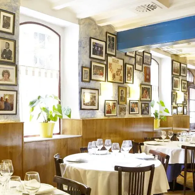 A hall with dozens of framed photographs on the wall and round tables in white cloths