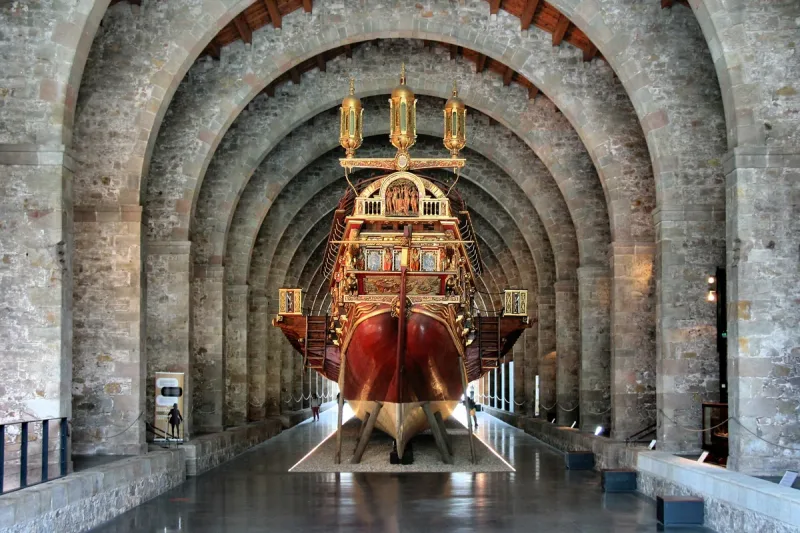 Gothic stone hall with arches and a gilded galley reconstruction