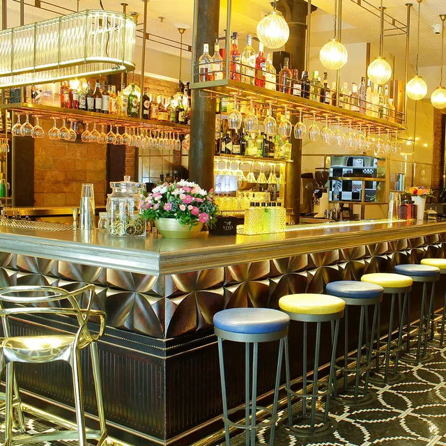 A long gilded bar with bottle shelves, glass pendant lamps and colourful stools