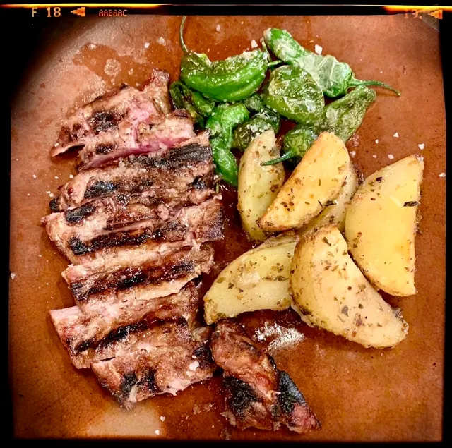 Sliced grilled meat beside potato wedges and small green peppers