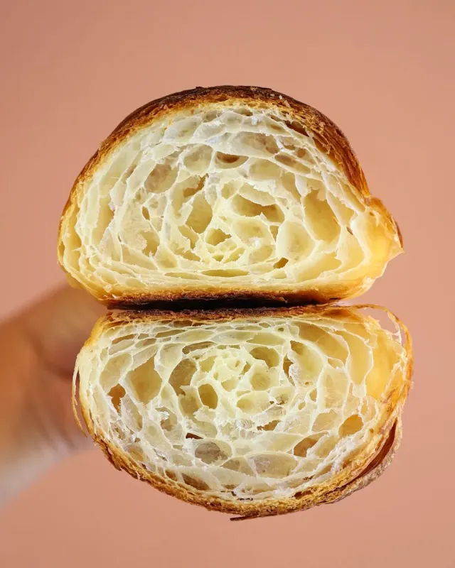 A croissant cut in two in close up, its inner crumb exposed, on a pink background