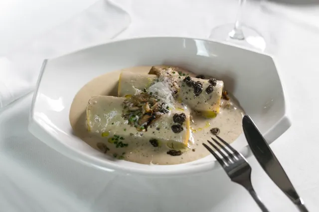 Pasta rolls in a cream sauce with mushrooms, in a white bowl on a white tablecloth