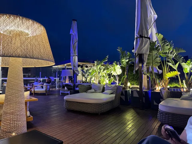 A roof terrace at night with wicker daybeds, tropical plants and a large woven lamp