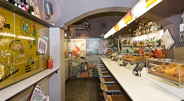 A narrow white counter with stools, pastries in a display case and hand drawn menu boards
