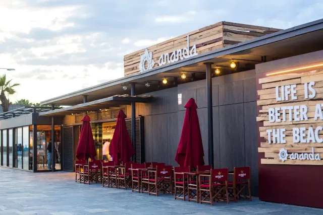 A wooden facade with closed red parasols and folding chairs, at dusk