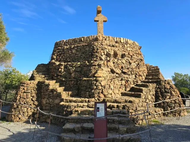 A stepped stone mound with a stone cross at its top, ringed by a rope barrier
