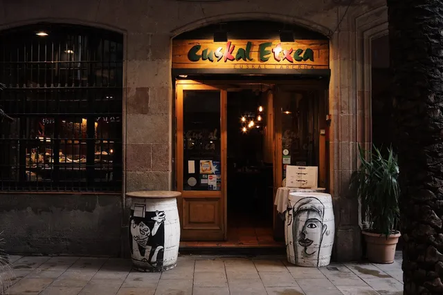 An entrance in a stone frontage with a wooden sign, and painted barrels on both sides of the door