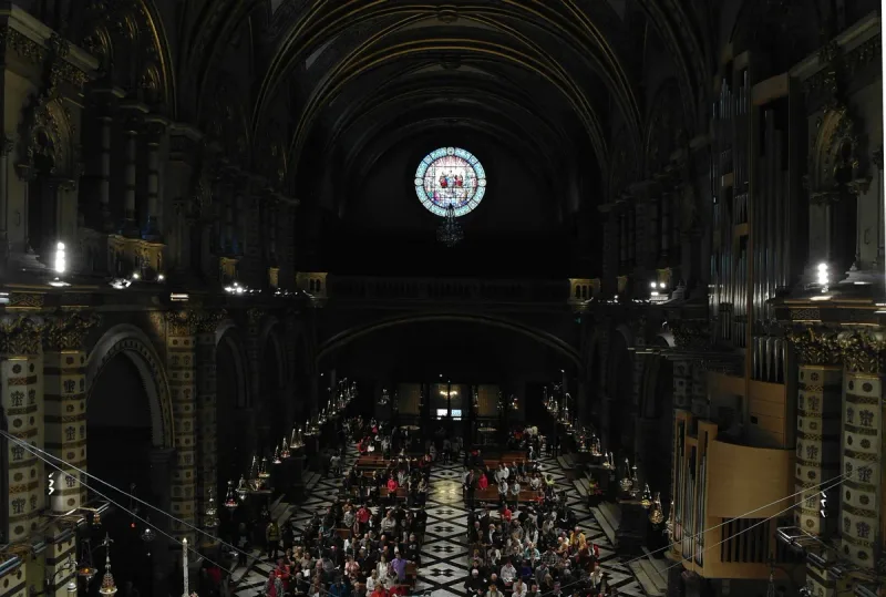 Dark basilica interior with a high vault, a round stained glass window and a crowd