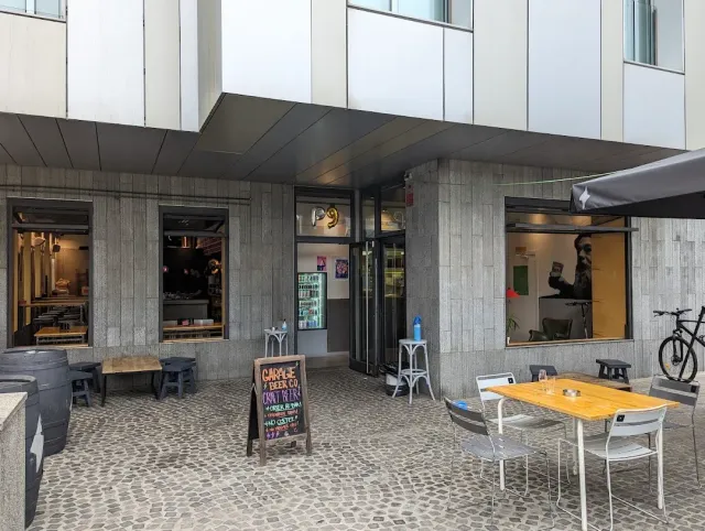 An entrance in a concrete building with a chalk sign, outdoor tables and a bicycle on a paved square
