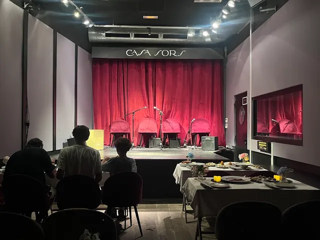 A stage with a red curtain, microphones and chairs, facing set tables and an audience