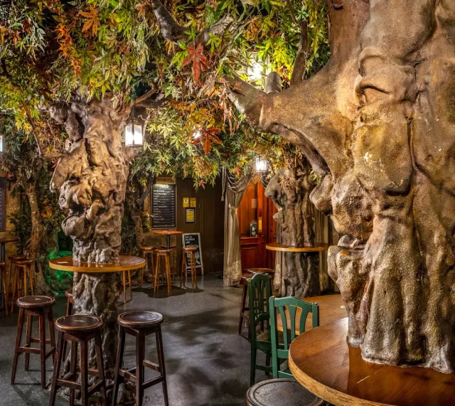 A space with artificial tree trunks, colorful hanging foliage and stools around