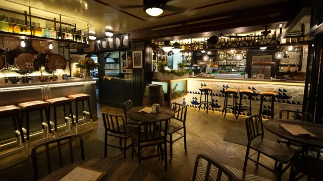 A hall with wooden barrels, high stools and round tables in warm lighting