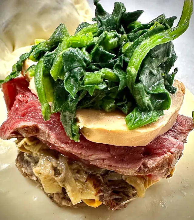 A layered dish with slices of pink meat, a pale slice and green leaves on top