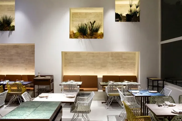 A bright hall with lit plant niches, an upholstered bench and mesh chairs