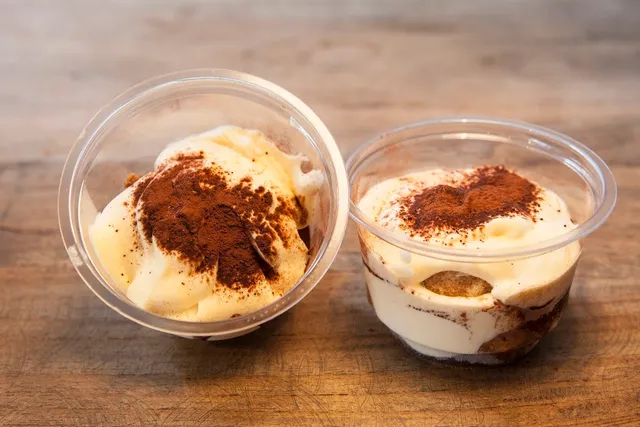 Two clear cups of creamy dessert dusted with cocoa powder on a wooden surface