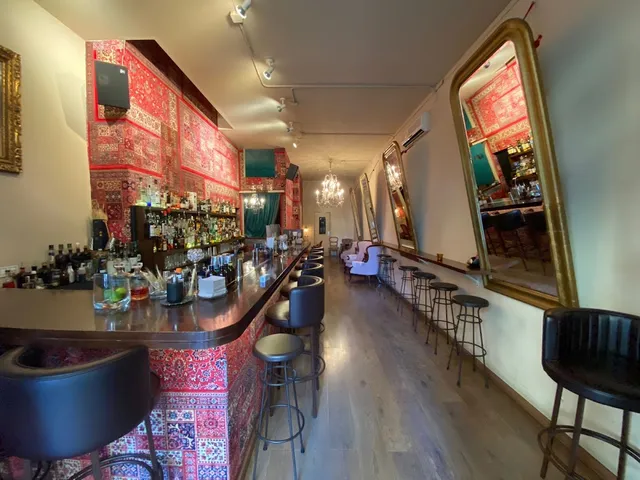 A long bar clad in red rugs, high stools and gilded mirrors on the wall
