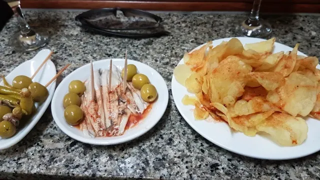 Three plates on marble: fish fillets with olives, pickles on a skewer and fried potato slices