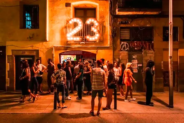 A crowd standing in the street at night before a lit facade with a numbered bulb sign