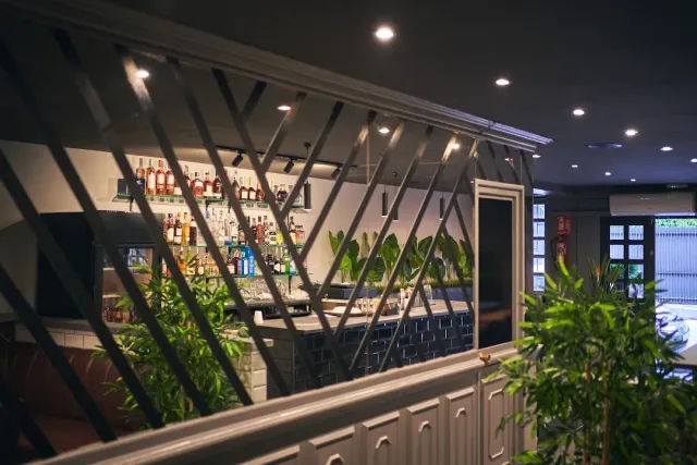 A view through a diagonal lattice toward a bar counter with bottle shelves and green plants