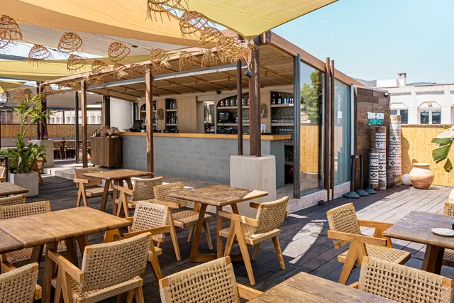 A wooden deck with woven chairs and tables under fabric awnings and wicker lamps