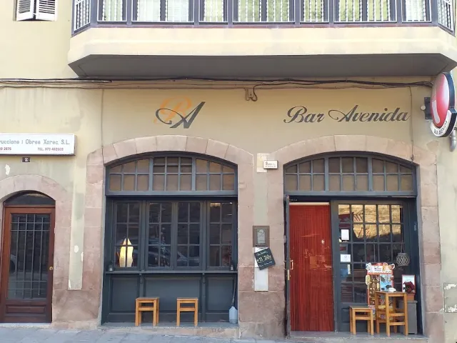 A facade with two arched windows, a handwritten sign and wooden stools on the pavement