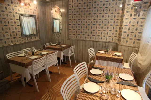 A room with blue patterned wallpaper, white chairs and checkered cloths on the tables