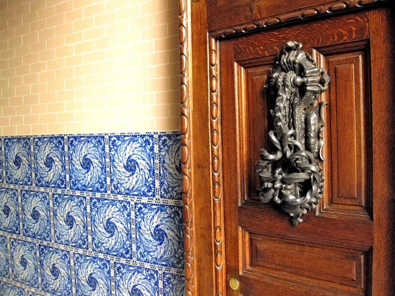 Heavy wooden door with an ornate iron knocker beside blue and white tiles