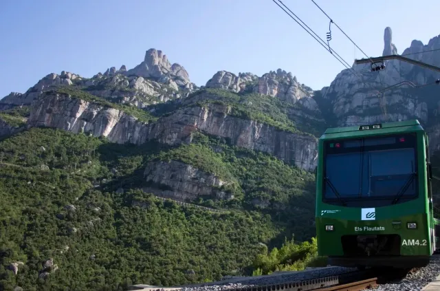 A green train car on the track, facing jagged rock peaks and green vegetation