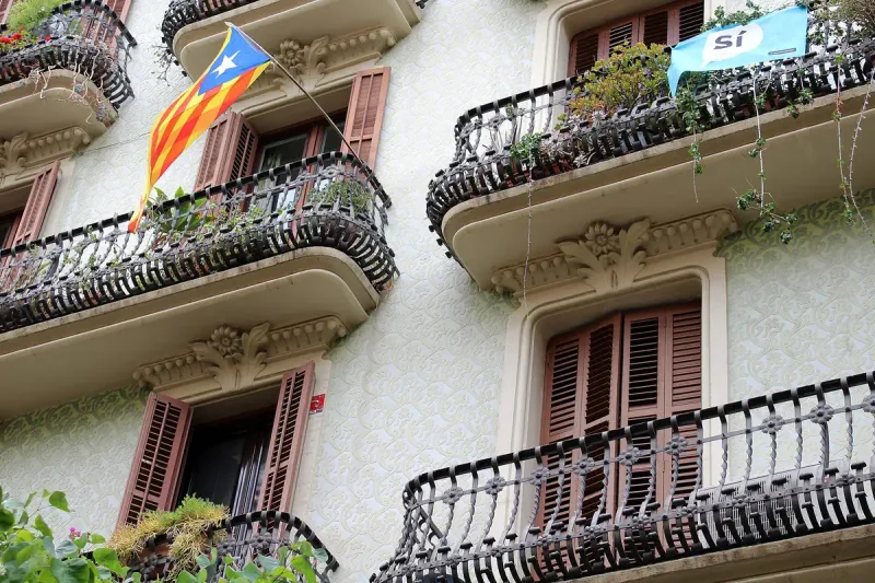 Iron balconies and pink shutters on a building facade with a Catalan flag