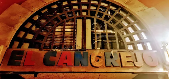 A sign in colorful letters beneath an arched window with a wooden lattice