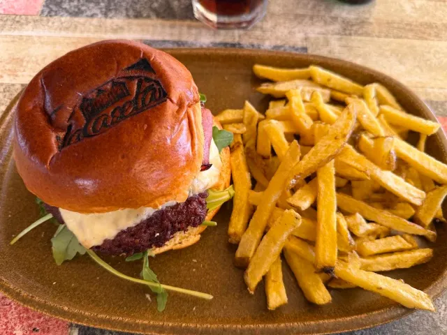 A meat sandwich in a stamped bun with melted cheese, beside fried potatoes