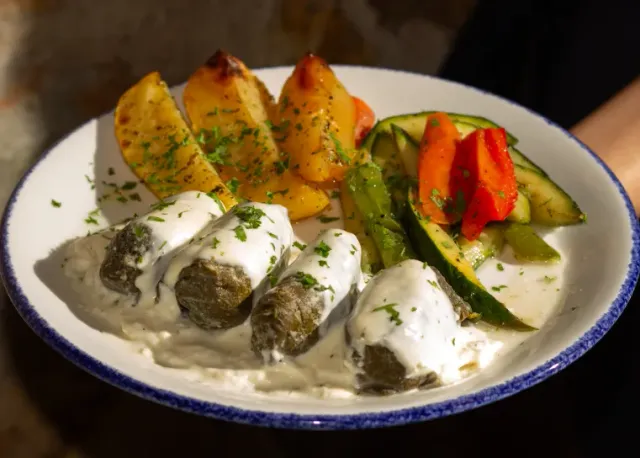 A plate with leaf rolls in white sauce, potato wedges and roasted vegetables