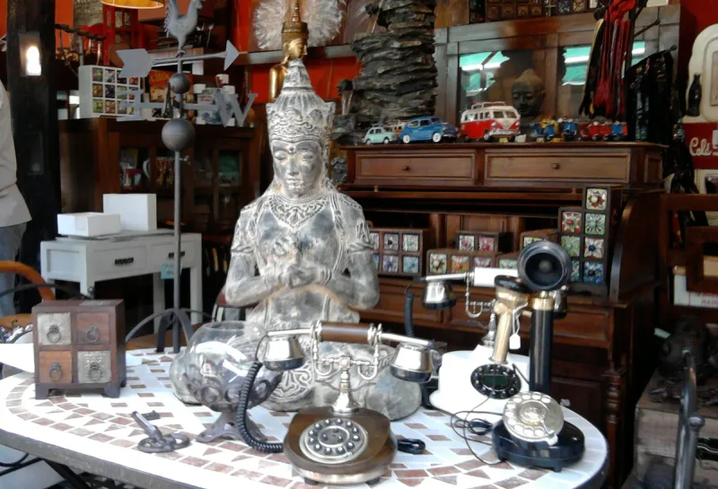 Flea market stall piled with silverware, old telephones and vintage objects