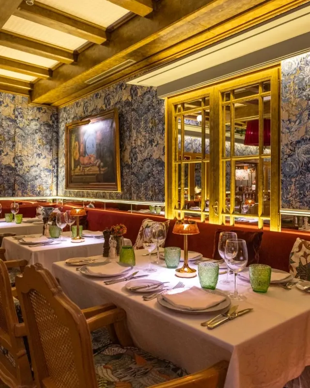A gilded dining hall with floral wallpaper, red banquettes and set tables